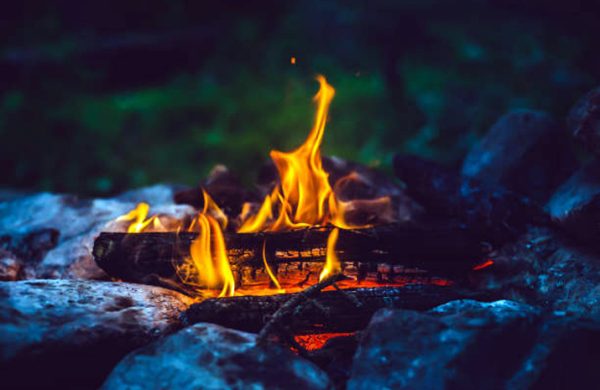 Vivid smoldered firewoods burned in fire close-up. Atmospheric warm background with orange flame of campfire. Unimaginable full frame image of bonfire. Burning logs in beautiful fire. Wonderful flame.
